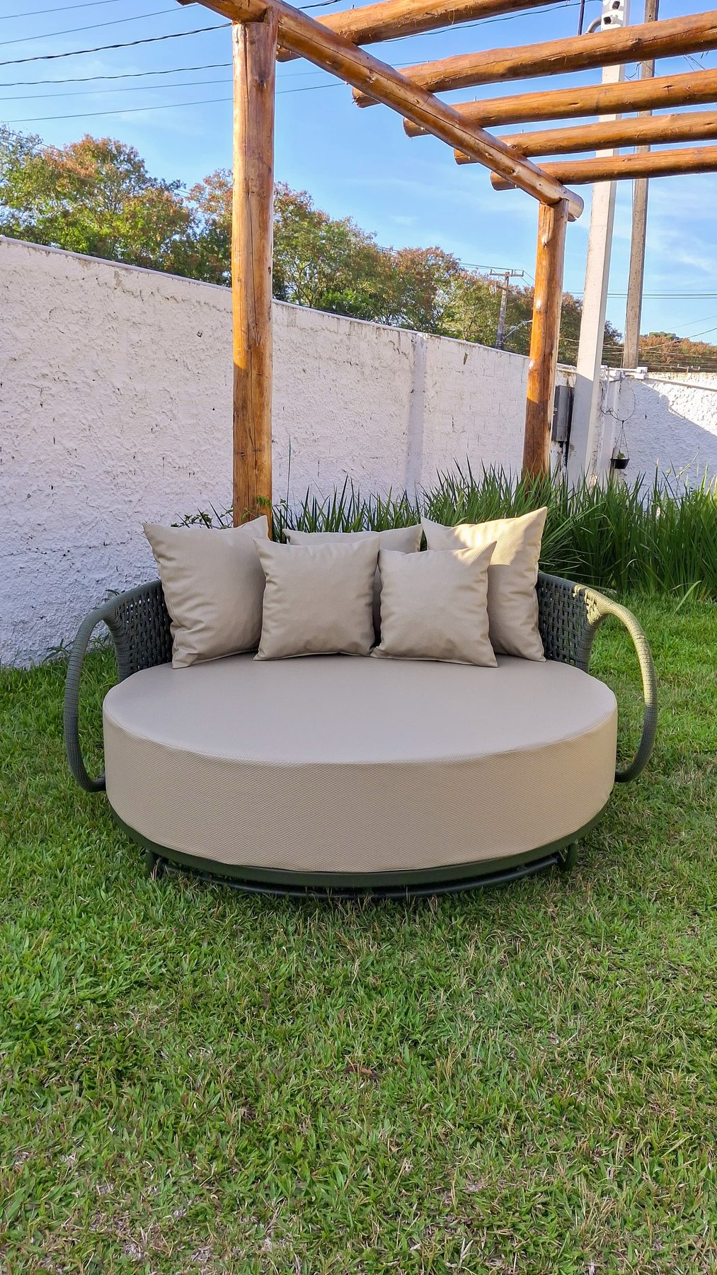Daybed circular com almofadas bege sob pergolado de madeira